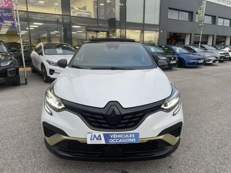 Vue avant d’un Renault Captur blanc nacré 2023, version hybride 1.6 E-Tech, avec calandre noire et détails dorés.