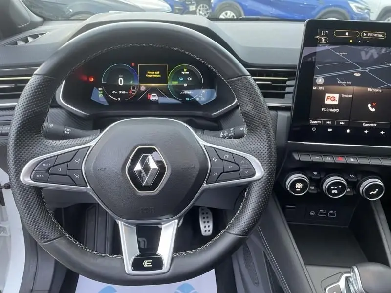 Vue intérieure centrée sur le volant noir perforé du Renault Captur blanc nacré 2023 avec tableau de bord numérique et écran tactile.