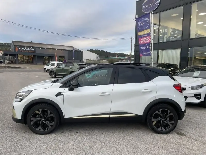 Profil côté gauche du Renault Captur 1.6 E-Tech hybride blanc nacré 2023 avec toit noir et jantes noires distinctives.