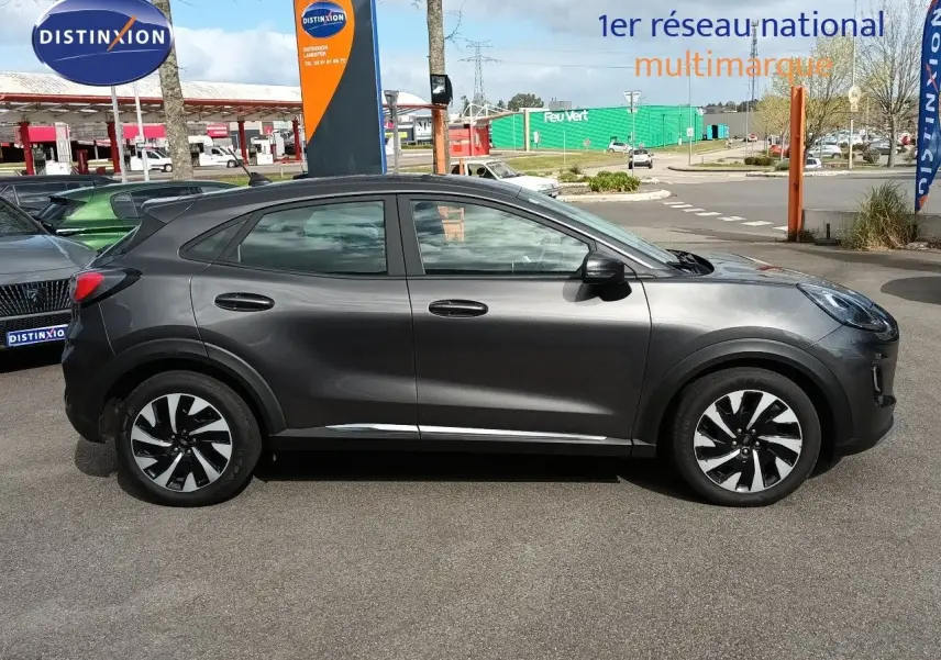 Vue de profil côté gauche d'une Ford Puma gris foncé métal, avec jantes bicolores et détails chromés sous les portes.