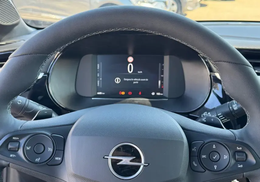 Vue rapprochée du volant noir de l’Opel Corsa rouge 2025 avec commandes intégrées et écran digital au tableau de bord.