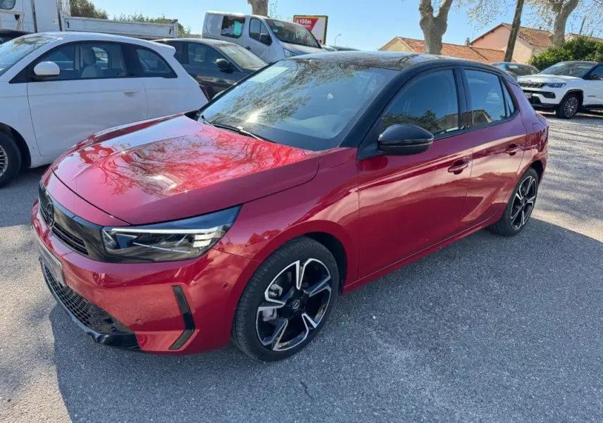 Opel Corsa rouge vue 3/4 avant droit, jantes alliage noires et toit noir brillant sous lumière naturelle.