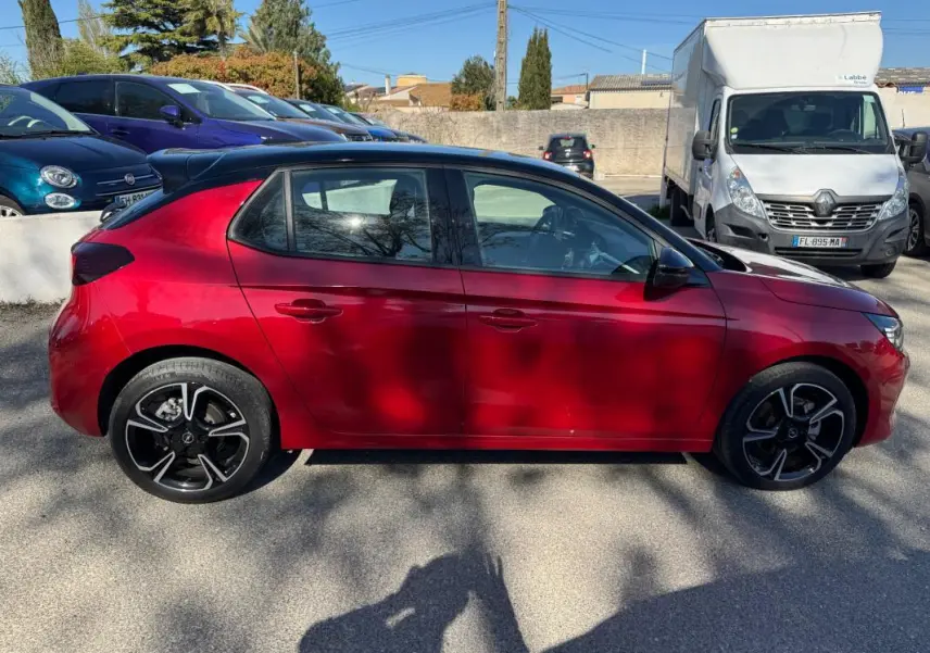 Vue latérale côté gauche d'une Opel Corsa rouge 2025 avec jantes alliage noires et toit noir.