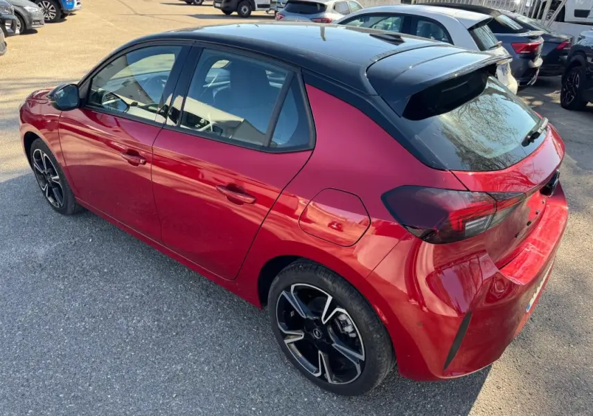 Vue 3/4 arrière droite d'une Opel Corsa rouge 2025 avec toit noir, jantes alliage 17 pouces et feux arrière fumés.