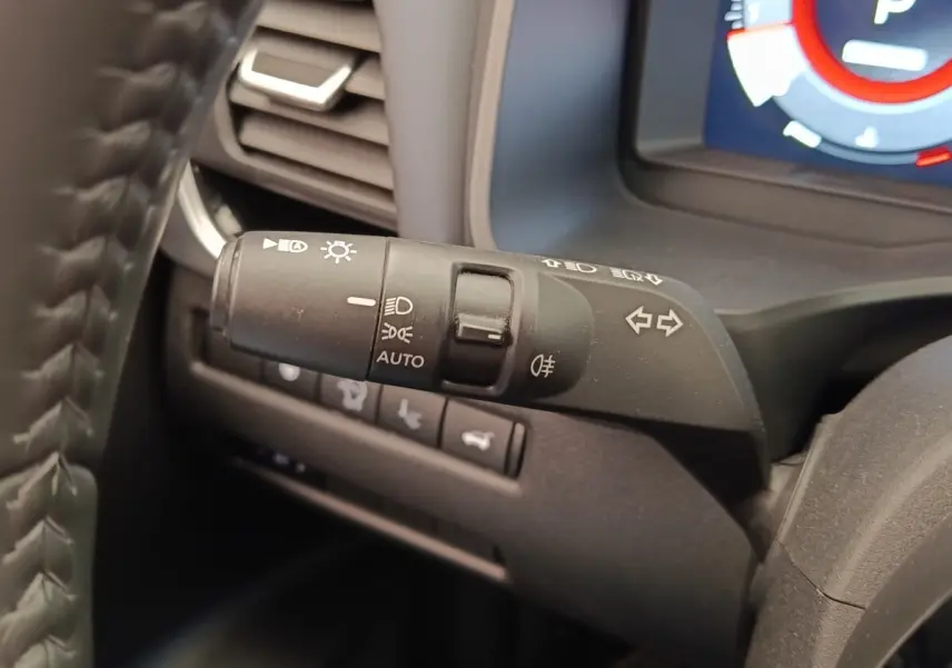 Gros plan sur la commande des phares et clignotants du Nissan Qashqai noir, avec tableau de bord numérique en arrière-plan.