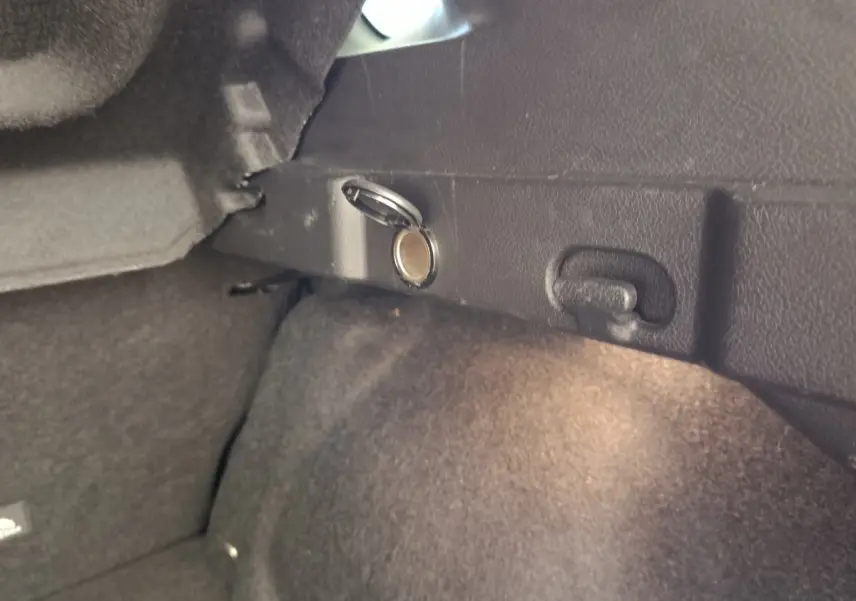 Détail intérieur du coffre du Nissan Qashqai 2023 noir, montrant une prise 12V avec couvercle ouvert.