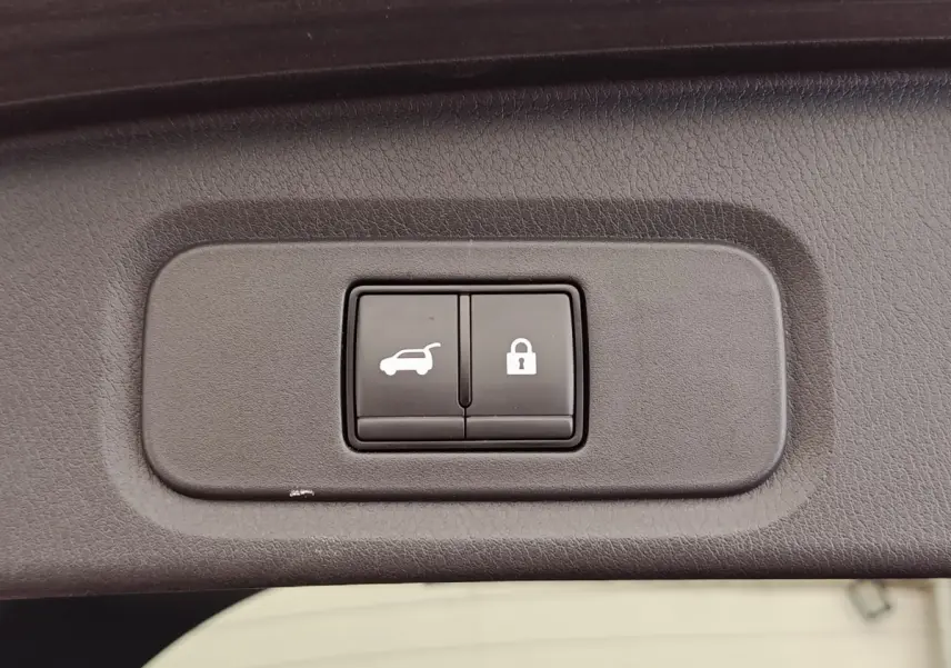 Boutons d'ouverture du coffre et de verrouillage intégrés dans le panneau intérieur du coffre d'un Nissan Qashqai noir.