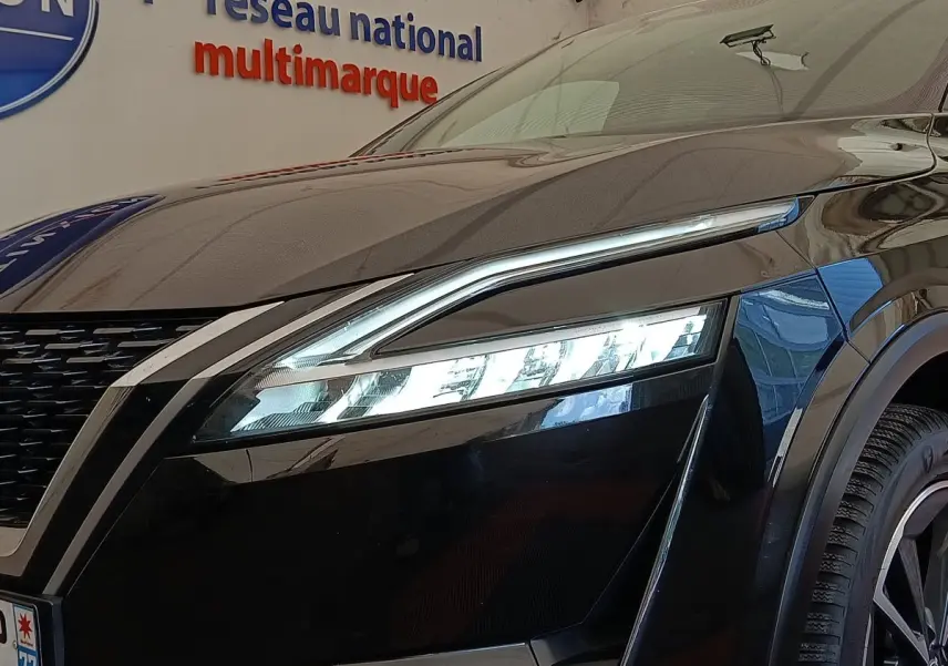Gros plan sur l'avant droit noir du Nissan Qashqai 2023, mettant en valeur le phare LED fin et la calandre distinctive.