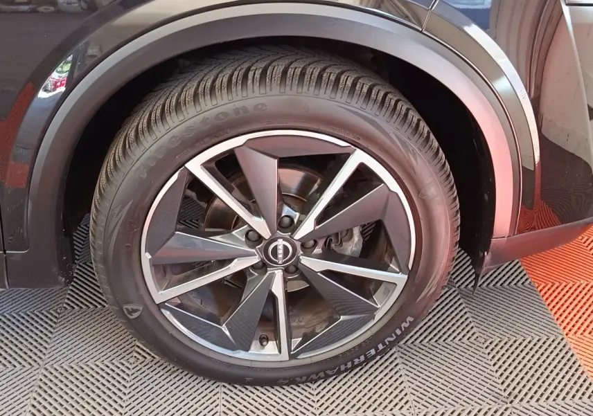 Gros plan sur la roue avant droite noire du Nissan Qashqai 2023 avec jante alliage et pneu Firestone.