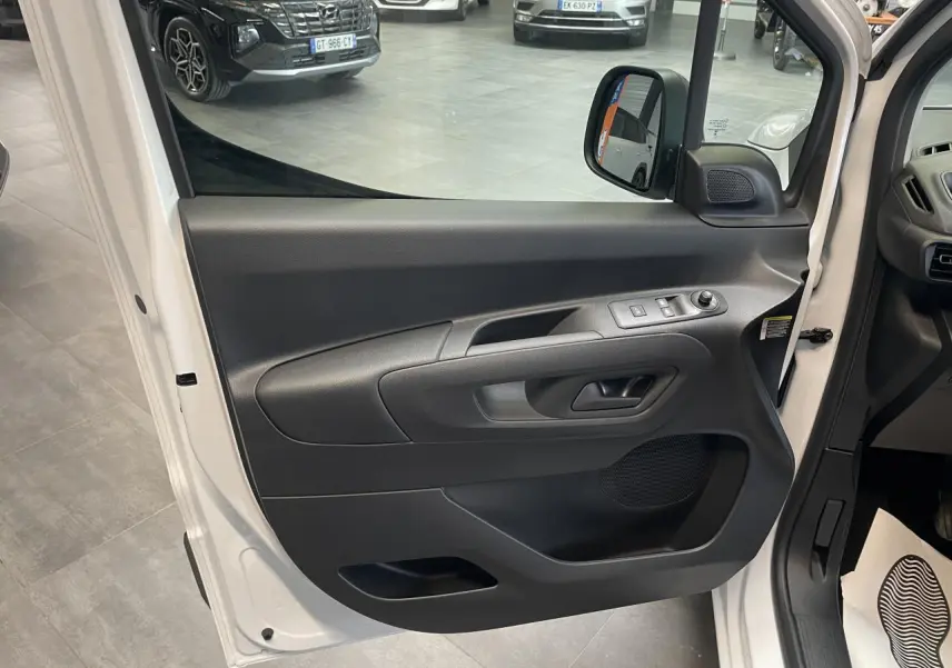 Vue rapprochée de la porte avant gauche blanche du Peugeot Partner 2026 avec commandes électriques et poignée noire.