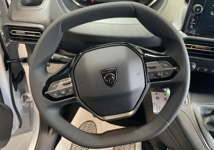 Vue rapprochée du volant multifonctions noir de la Peugeot Partner blanche, avec tableau de bord et levier de vitesses visibles.