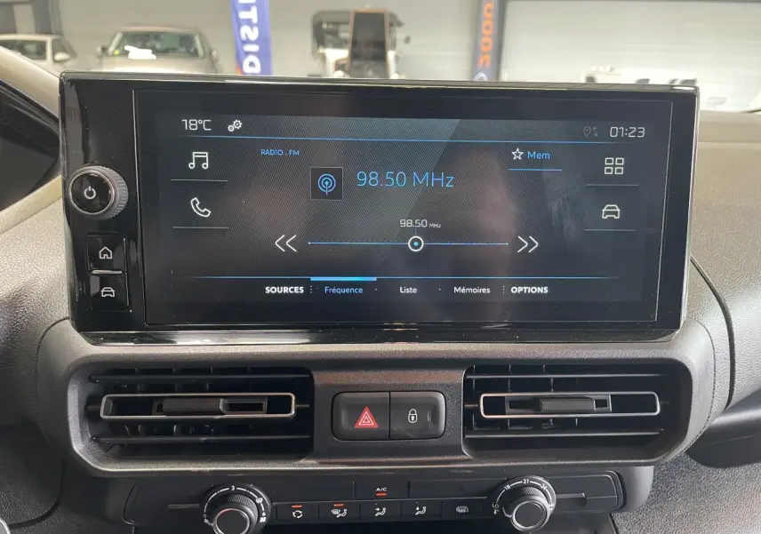 Vue intérieure du tableau de bord du Peugeot Partner blanc, avec écran tactile central affichant la radio FM à 98,50 MHz.