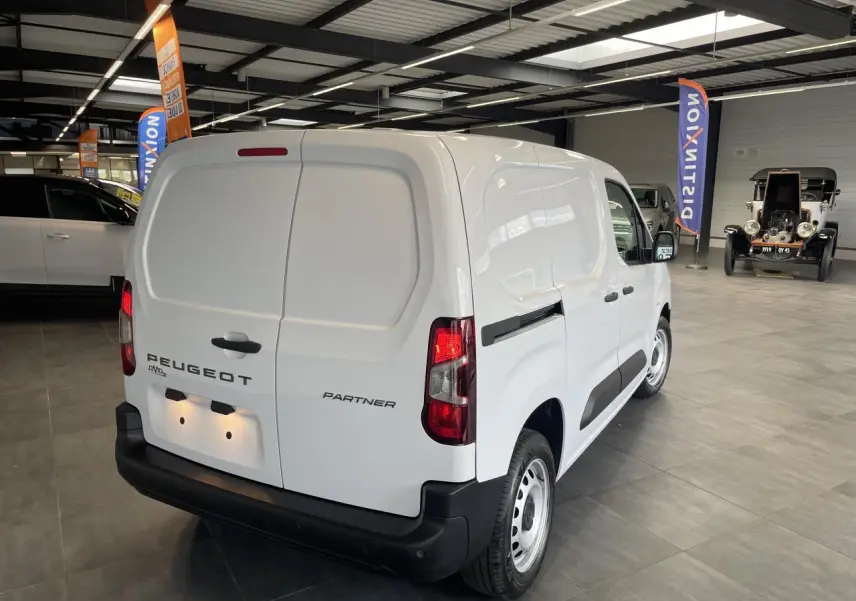 Vue 3/4 arrière droite du Peugeot Partner blanc, fourgon utilitaire en intérieur avec portes arrière battantes fermées.
