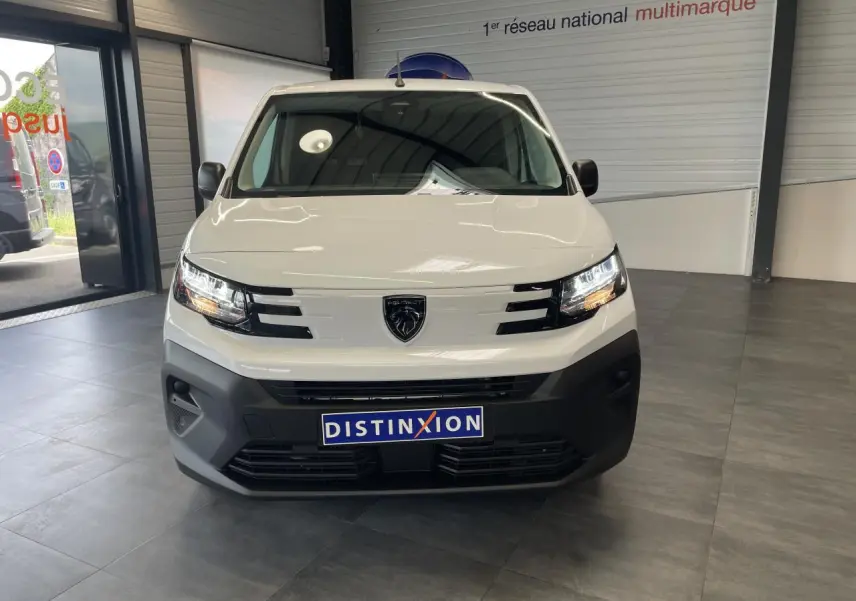 Vue frontale d’un utilitaire Peugeot Partner blanc avec calandre noire et logo lion au centre, en intérieur showroom.