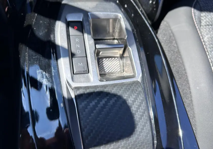 Gros plan sur la console centrale noire brillante du Peugeot 2008 Hybrid 136 e-DCS6 Allure avec sélecteur de boîte auto.