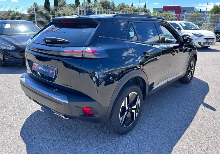 Vue 3/4 arrière droite d’un Peugeot 2008 Hybrid noir avec barres de toit et jantes alliage 17 pouces brillantes.