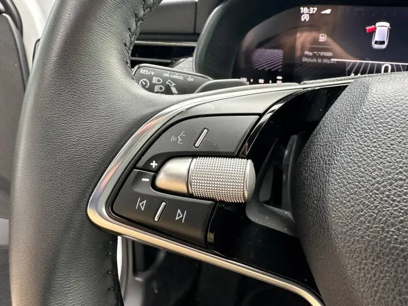 Gros plan sur les commandes audio au volant cuir noir d'une Skoda Scala blanche, avec écran numérique en arrière-plan.