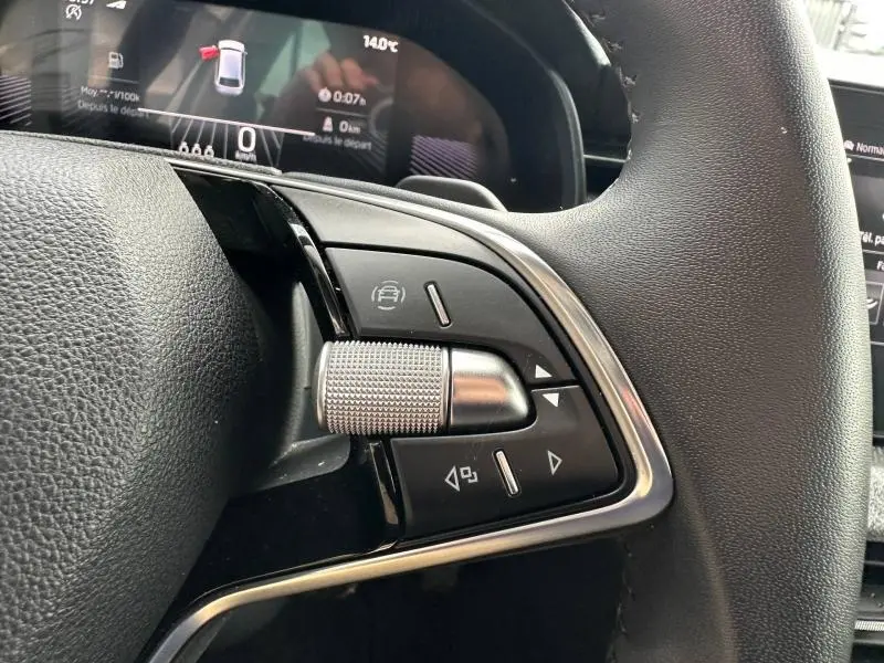 Gros plan sur les commandes multifonctions côté gauche du volant cuir noir de la Skoda Scala blanc cristal, avec molette métallique texturée.