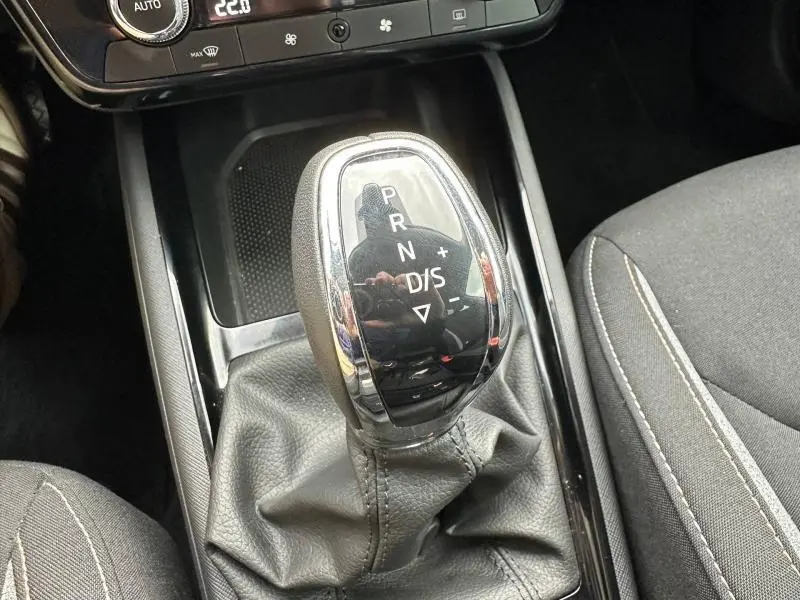 Gros plan sur le levier de vitesses automatique noir et chrome de la Skoda Scala blanc cristal, avec coutures visibles sur les sièges gris.