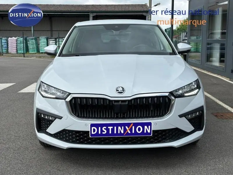 Vue avant d'une Skoda Scala blanc cristal avec calandre noire et phares LED, sur parking extérieur devant bâtiment.