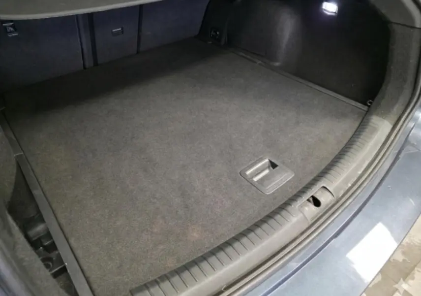Coffre ouvert vu de dessus du CUPRA Leon Sportstourer gris, avec tapis de sol noir et éclairage intérieur.