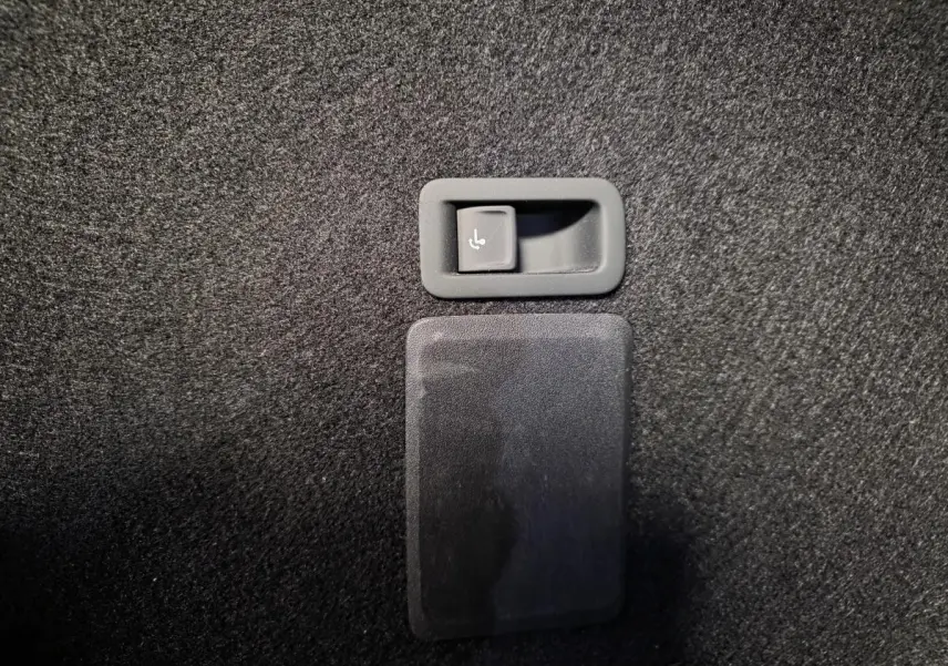 Détail du bouton de rabattement électrique des sièges arrière sur la moquette noire du coffre du CUPRA Leon Sportstourer gris.