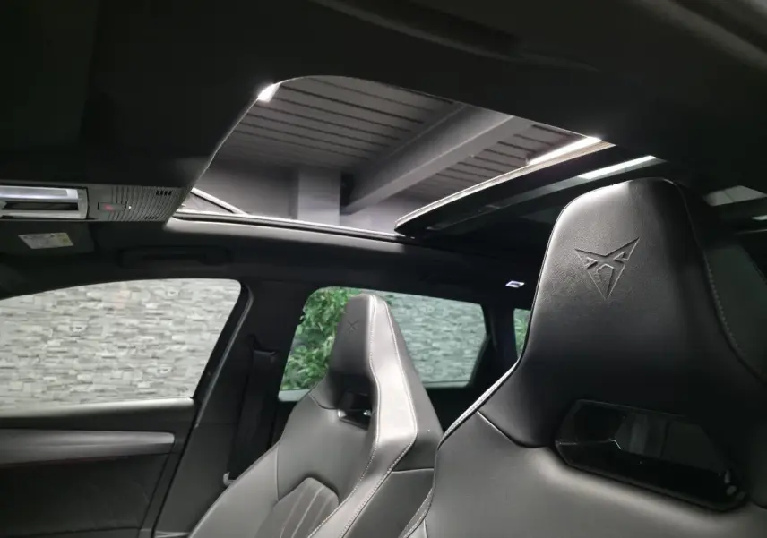 Vue intérieure montrant les sièges baquets noirs avec logo Cupra et le toit ouvrant panoramique ouvert.
