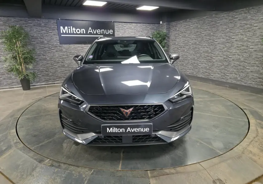 Vue avant d'une CUPRA Leon Sportstourer gris magnétique, avec calandre noire et logo cuivre, en intérieur showroom.