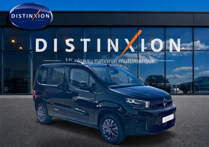 Vue 3/4 avant droite du Citroën Berlingo noir, avec barres de toit et jantes alu, devant une vitrine Distinxion.