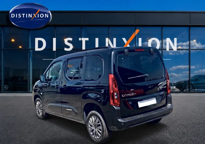 Vue 3/4 arrière droite du Citroën Berlingo noir avec barres de toit et vitres arrière teintées, devant un bâtiment Distinxion.