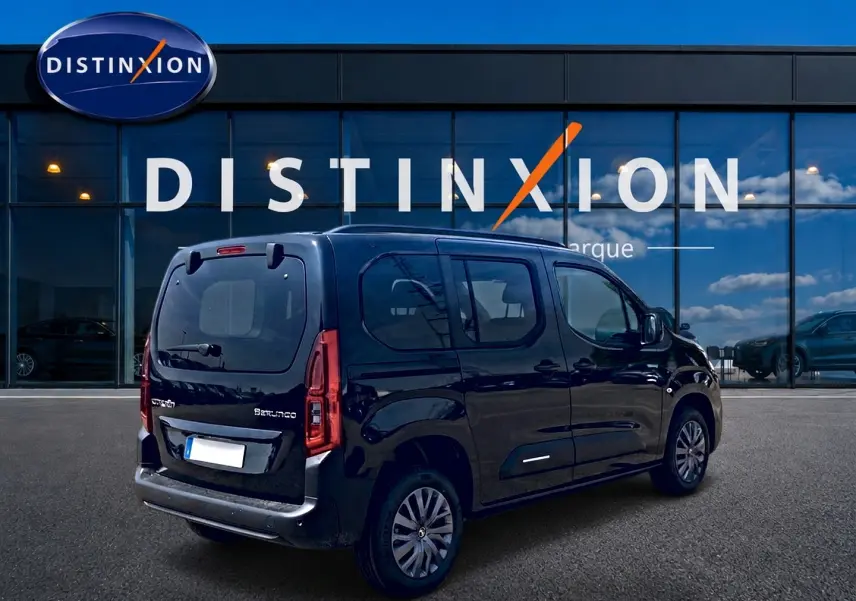 Vue 3/4 arrière droite d’un Citroën Berlingo noir 2026 avec barres de toit et vitres teintées, devant un showroom Distinxion.