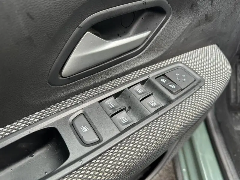 Gros plan sur la commande des vitres électriques et la poignée intérieure côté conducteur du Dacia Jogger 2025 couleur Kaki Lichen.