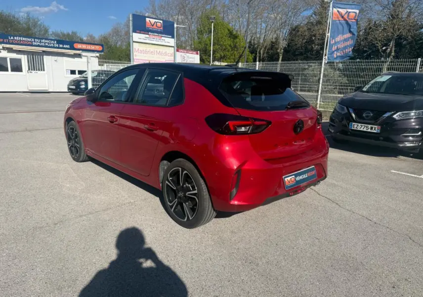 Vue 3/4 arrière droite d'une Opel Corsa rouge 2025 avec toit noir et jantes alliage noires, stationnée en extérieur.