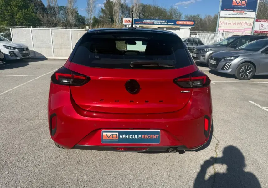 Vue arrière d'une Opel Corsa rouge 2025 hybride, avec feux arrière modernes et badge "Hybrid" visible.