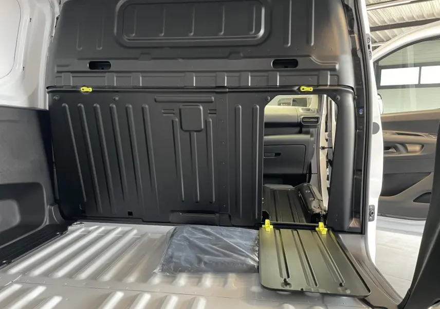 Vue intérieure du fourgon blanc Peugeot Partner 2026, montrant la cloison pleine fixe et la banquette passager rabattue avec tablette écritoire.