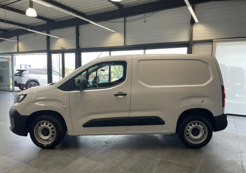 Vue de profil côté gauche d’un Peugeot Partner blanc en fourgon, avec jantes tôles grises et protections noires sur les portières.