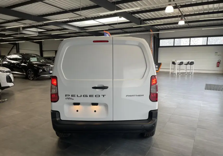 Vue arrière d'un Peugeot Partner blanc stationné en intérieur, avec portes battantes fermées et feux allumés.