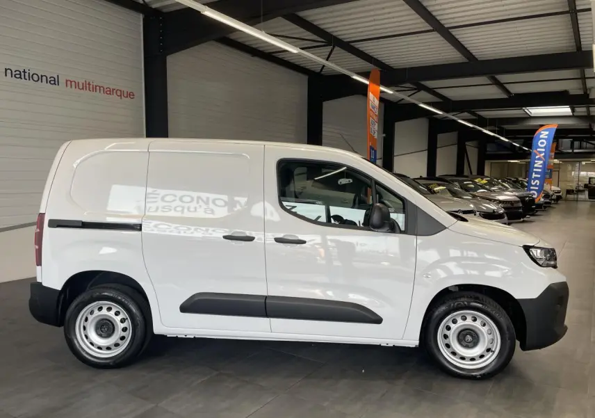 Vue de profil côté droit d’un Peugeot Partner blanc en fourgon dans un showroom, avec jantes tôles grises et porte latérale coulissante.