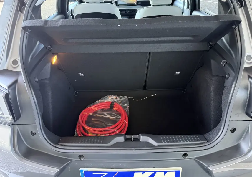Coffre ouvert vue arrière d'une Citroën E-C3 113 MAX gris Mercury avec câble de recharge électrique rouge visible.