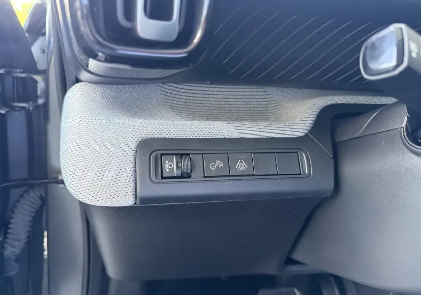 Vue intérieure du tableau de bord côté gauche de la Citroën C3 E-C3 113 MAX 2025 avec sellerie tissu clair et commandes d'éclairage.