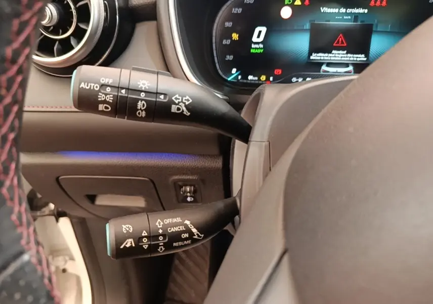 Gros plan sur le volant et les commandes de clignotants et régulateur de vitesse du MG Motor EHS hybride blanc, tableau de bord digital.