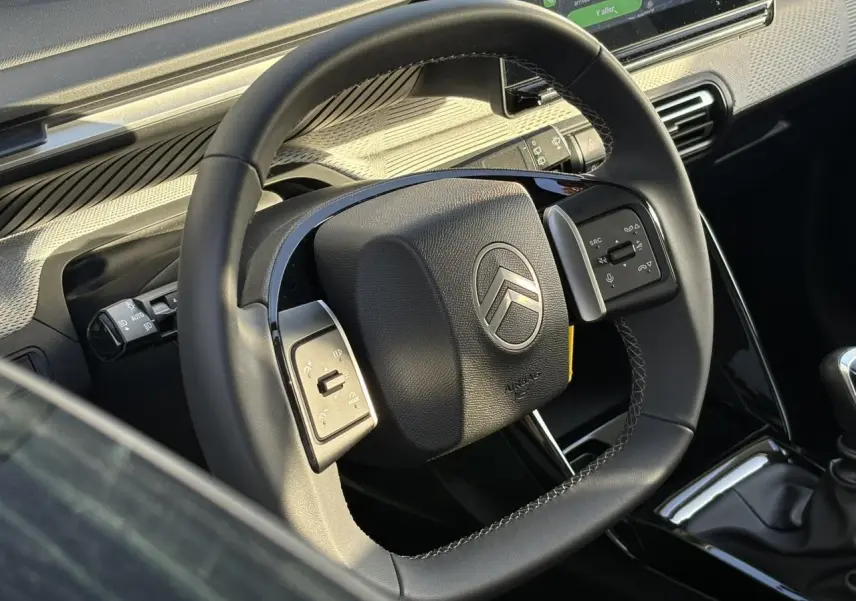 Gros plan sur le volant noir de la Citroën C3 2025 avec commandes intégrées et tableau de bord en arrière-plan.