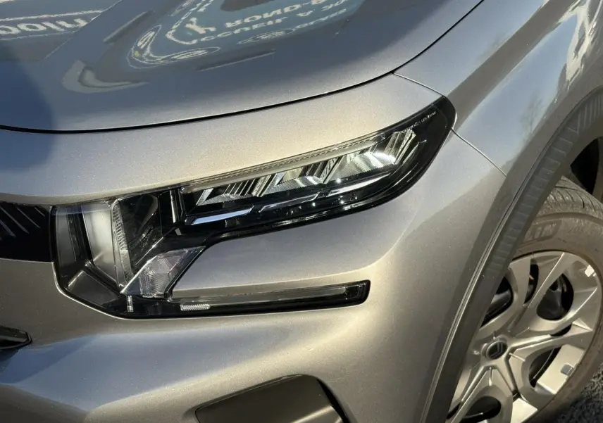 Gros plan sur le phare avant droit et la roue d’une Citroën C3 2025 gris Mercury avec toit noir.