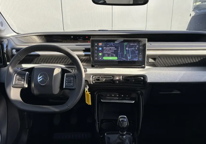 Vue intérieure frontale du tableau de bord de la Citroën C3 2025 avec volant, écran GPS 10 pouces et levier de vitesses manuel.