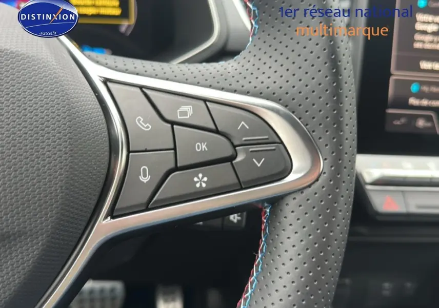 Gros plan sur les commandes multifonctions du volant cuir perforé du Renault Captur 1.8 e-tech hybride bleu iron t/noir.