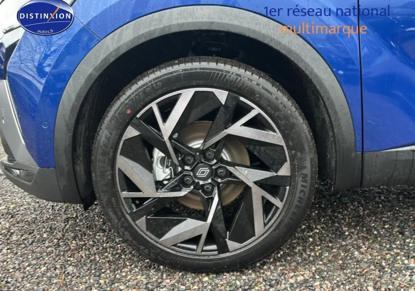 Gros plan sur la roue avant droite du Renault Captur bleu iron avec jante alu noire et argentée au design géométrique.