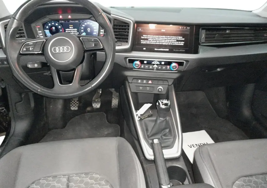 Vue rapprochée de l'écran tactile central de l'Audi A1 Sportback 2023, avec interface multimédia et commandes climatisation visibles.