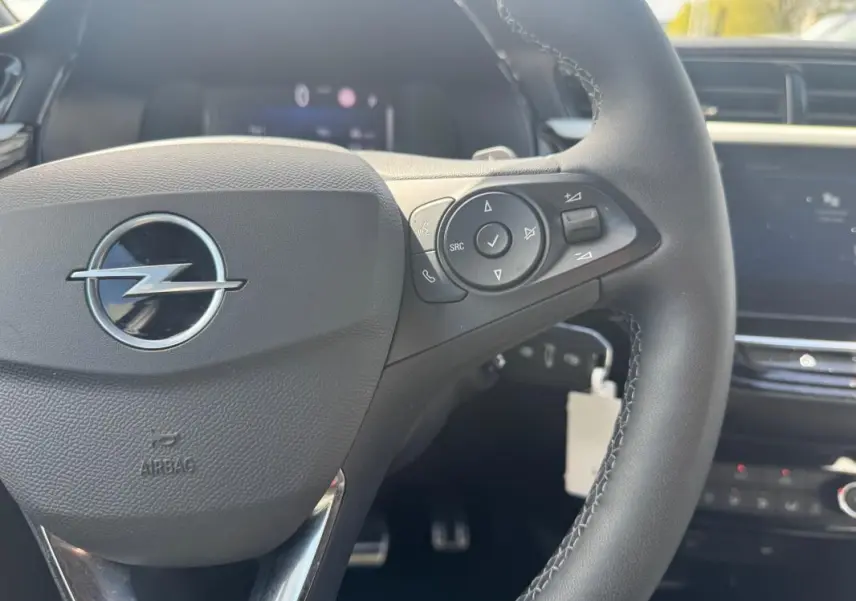 Vue rapprochée du volant multifonctions noir de l’Opel Corsa 2025 avec commandes audio et tableau de bord flou.
