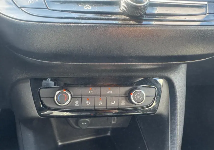 Vue rapprochée de la console centrale de l’Opel Corsa noire, montrant les commandes de climatisation manuelle et prises 12V et USB.