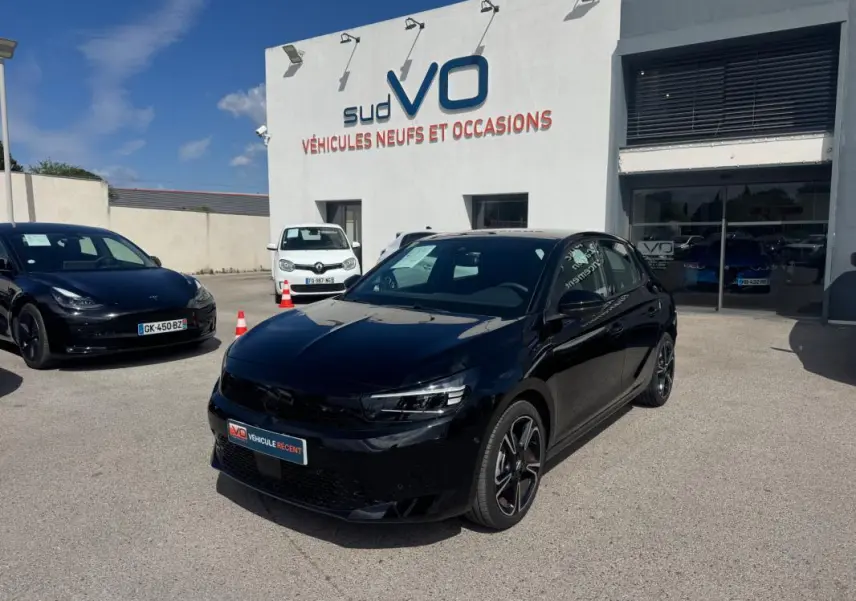 Opel Corsa 1.2 Turbo Hybrid noir vue 3/4 avant droit avec jantes alliage 17 pouces, stationnée devant un garage.